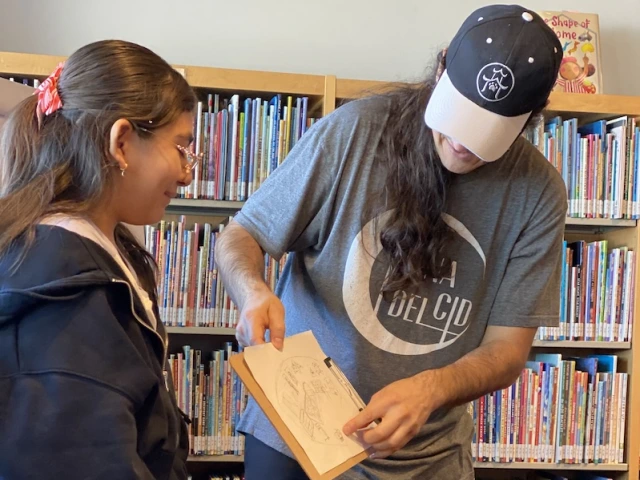 A Middle School Reading Ambassador shares her sketch with author and illustrator, Jose Pimienta, at a cartooning workshop run by the artist.