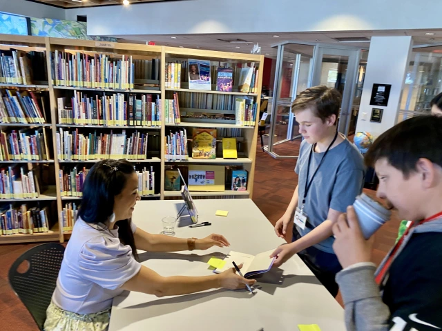 woman signs books for middle schoolers