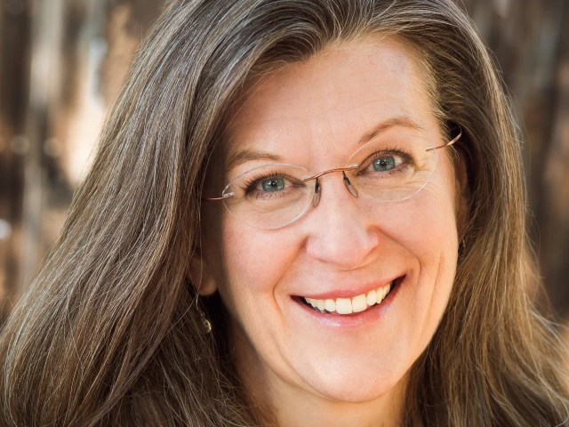A woman with brown hair and glasses smiles at the camera.