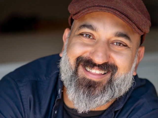 Daniel Nayeri, an Iranian-American man, smiles at the camera. He has a black mustache that trails into a gray beard.