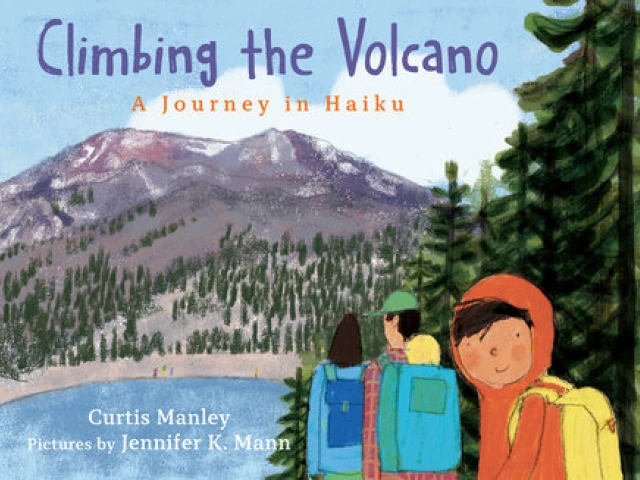 A young boy smiles at the viewer as he hikes with his parents to a mountain.