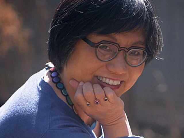 An Asian woman with short hair and glasses smiles at the camera.