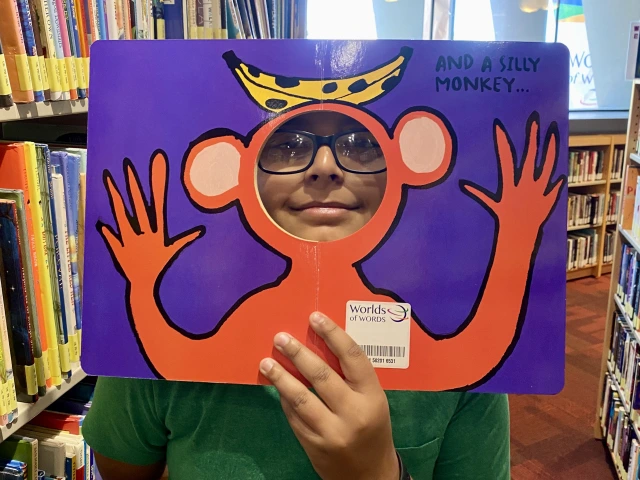 Middle school boy in glasses peeks through a book die cut of a silly monkey.