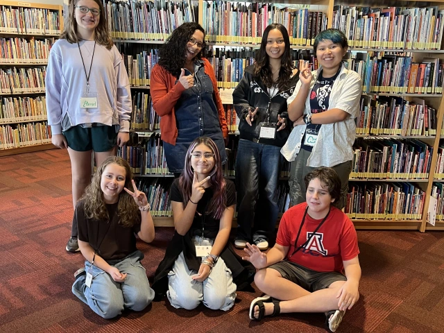 Six middle schoolers smile while gesturing with peace signs as they pose with an adult author