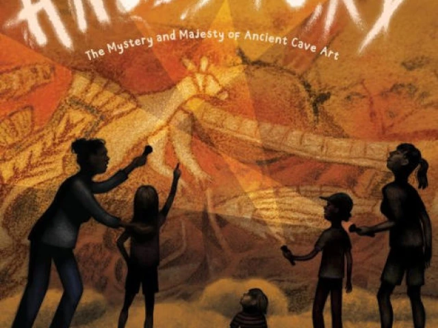 A group of people looking up at cave drawings, illuminated by flashlights.