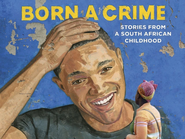 Street art of a portrait of Trevor Noah smiling with a hand on his head as a woman walks by.