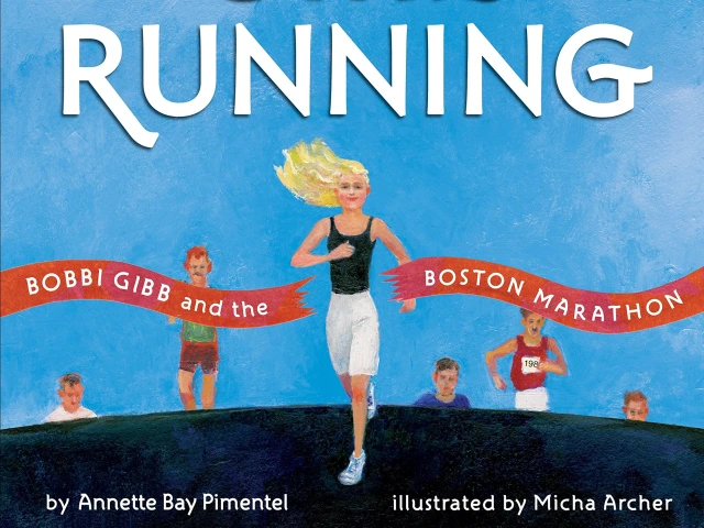 A blonde woman running a marathon and crossing the red ribbon finish line.