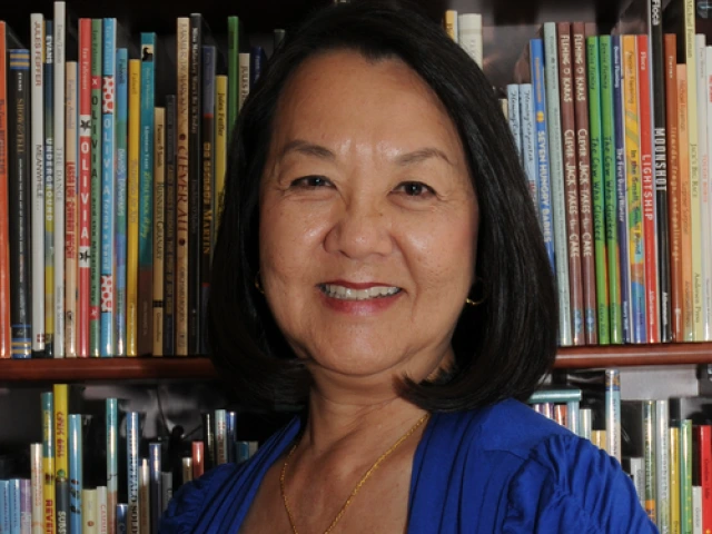 A smiling Mary J. Wong posed in front of a shelf with many picturebooks.