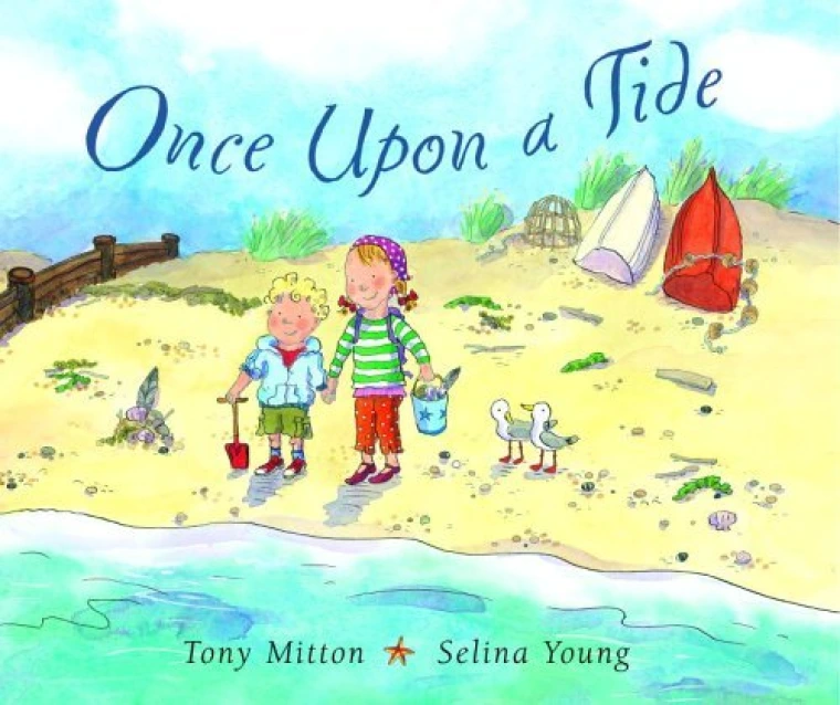 Two children stand on a beach with a bucket and shovel.