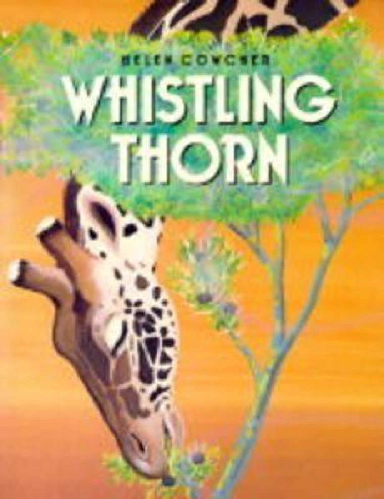 A giraffe leans down from above the cover to eat leaves off a bush.