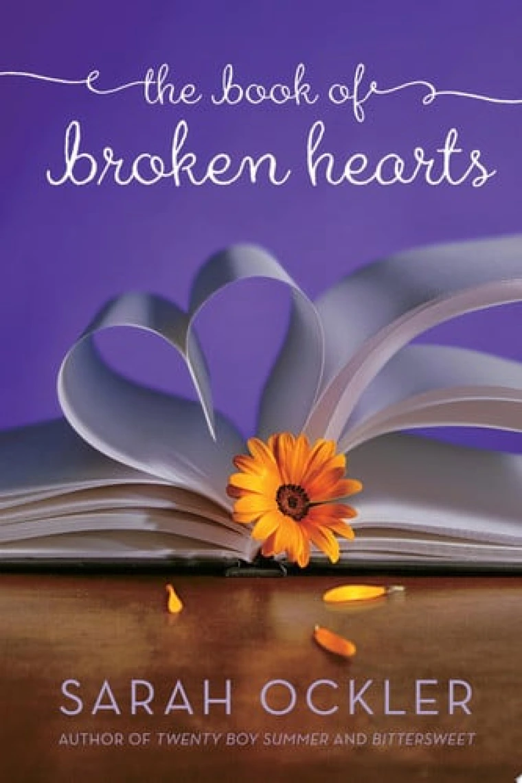 A book is laid flat with its pages folded into a heart and in between the pages pokes out a flower