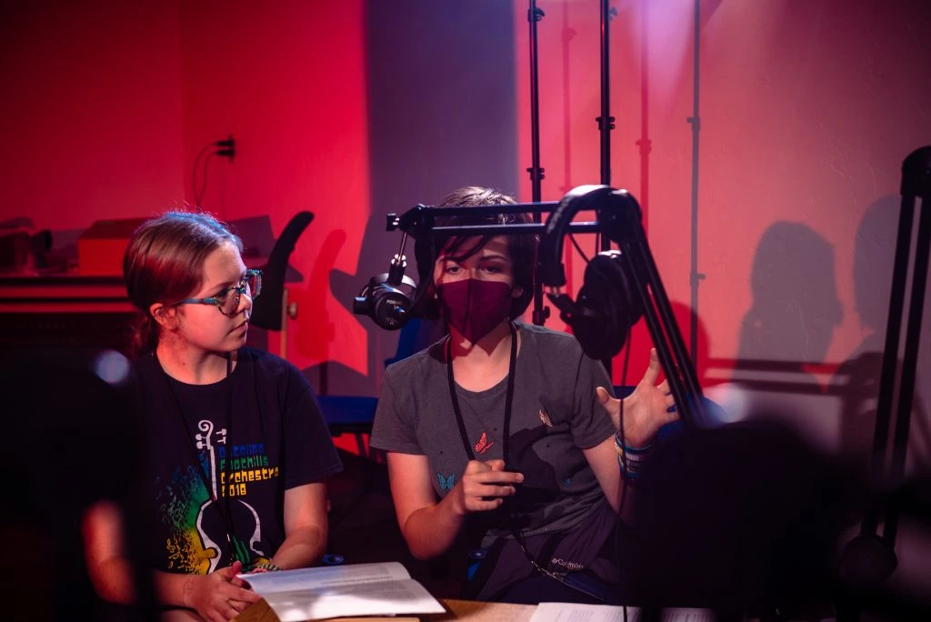 Two young adults sitting in front of podcast microphones