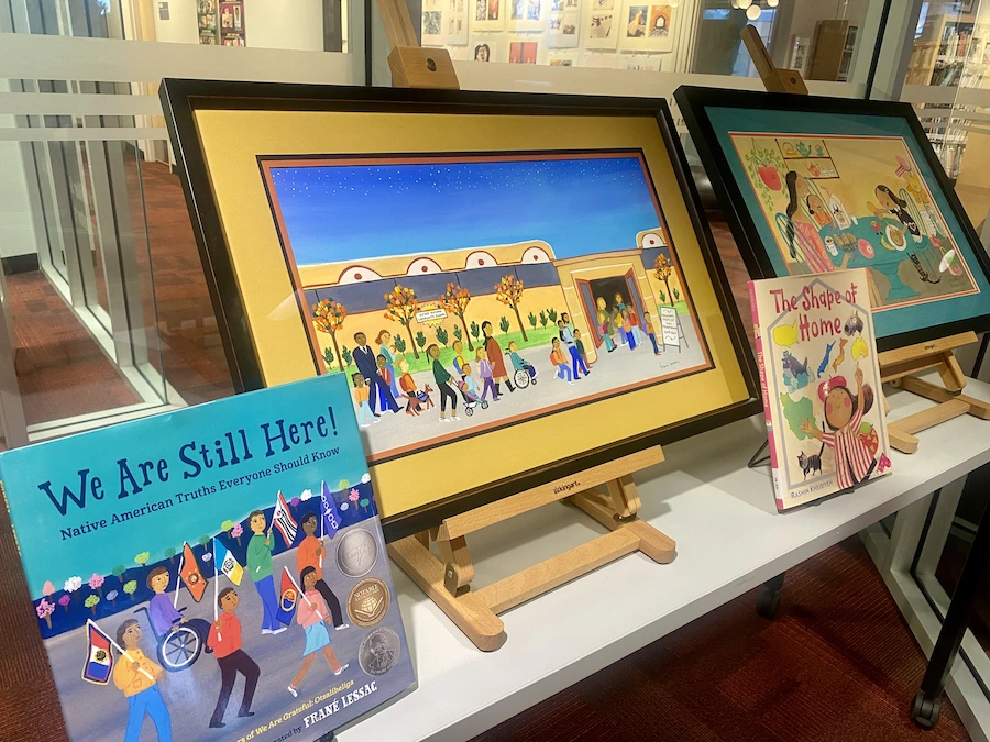 To framed art pieces on table easels accompanied by their paired book