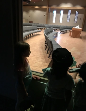 Children standing in the nursery, looking through the one-way glass window into the church