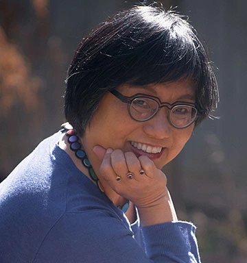 An Asian woman with short hair and glasses smiles at the camera.