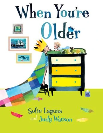 Boy with a crown and patchwork cape stands on a stool to see his baby brother on a dresser changing table. 