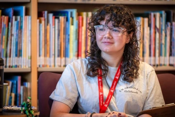 Teen girl with curly hair and a U of A COE lanyard on listens to a presentation