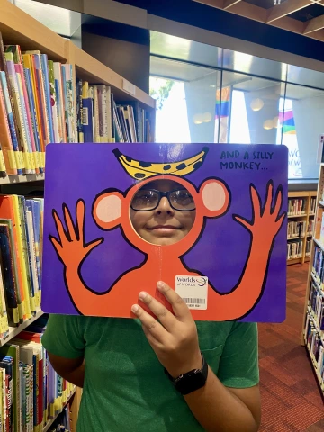 Middle school boy in glasses peeks through a book die cut of a silly monkey.