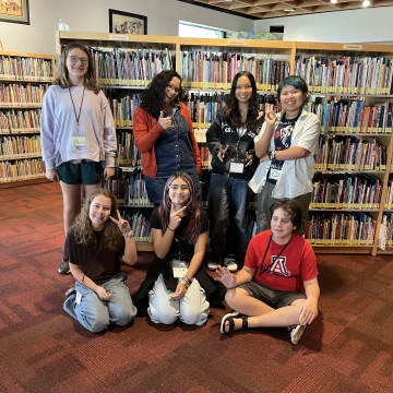 Six middle schoolers smile while gesturing with peace signs as they pose with an adult author