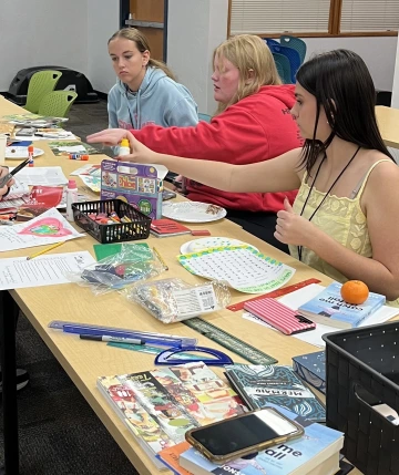 Three teens working at a table piled with art supplies.