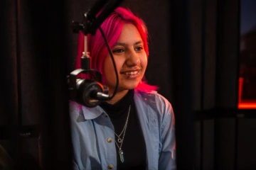 Teen with pink hair smiles into a microphone