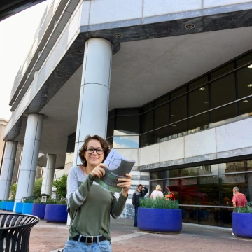 A Teen Reading Ambassador holds up book flyers in front of a public library.