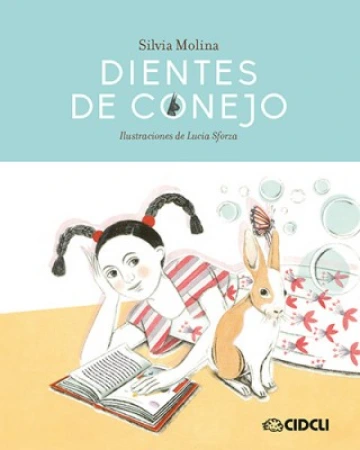 Cover of dientes de conejo depicting a young girl with black braided pigtails laying on the floor besides a bunny, reading a book.