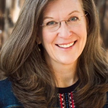 A woman with brown hair and glasses smiles at the camera.