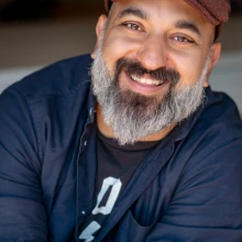 Daniel Nayeri, an Iranian-American man, smiles at the camera. He has a black mustache that trails into a gray beard.