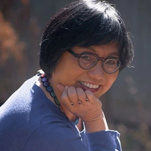 An Asian woman with short hair and glasses smiles at the camera.