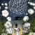 Cover of Midnight Without A Moon depticing a black girl in a white dress facing away from the viewer, surrounded by white flowers and looking towards the sihlouette of a house in the background with the lights in the windows illuminated.