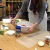 Image of a teacher in a white apron mixing ingredients into a white plastic bowl on a wooden table. There is a sheet of plastic besides the bown and various bottles of spices on the table.