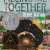 Cover of Piecing Me Together depicting a black girl with a colorful headband standing before a colorful background of trees and houses.