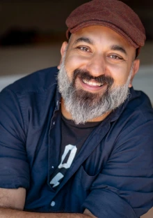 Daniel Nayeri, an Iranian-American man, smiles at the camera. He has a black mustache that trails into a gray beard.