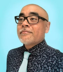 A bald man with glasses wears a floral patterned shirt with a tie.
