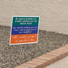 A sign reading "No matter where you're from, we're glad you're our neighbor" in Spanish, English, and Arabic on a green, blue, and orange background