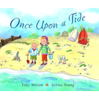 Two children stand on a beach with a bucket and shovel.