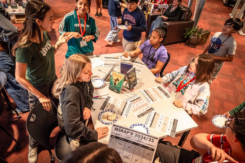 Middle Schoolers gather around a table for games, food, and books.