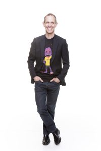 Full-length shot of Andy Griffiths in dark jeans and a blazer over a graphic T-shirt.