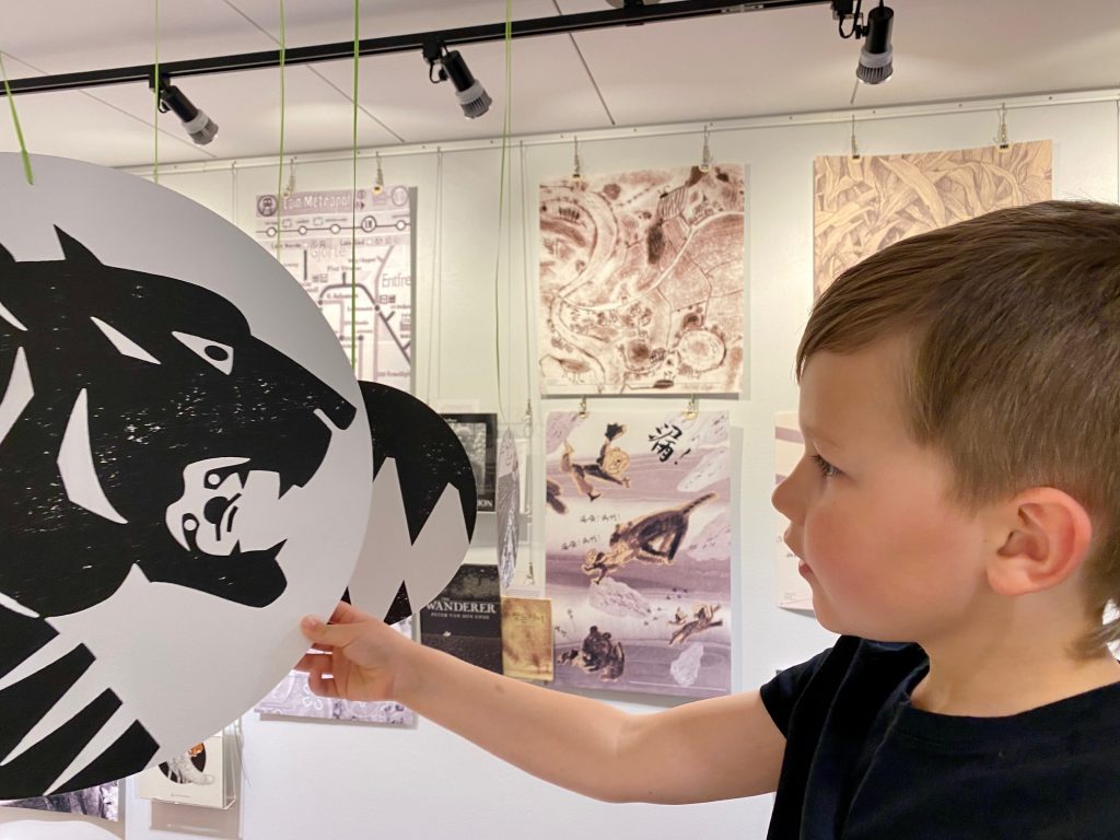 A young boy holds a hanging sign from the Black White Grey Exhibit that depicts a tiger with a sloth in its mouth.