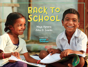 Two smiling children sit on the floor as they do schoolwork