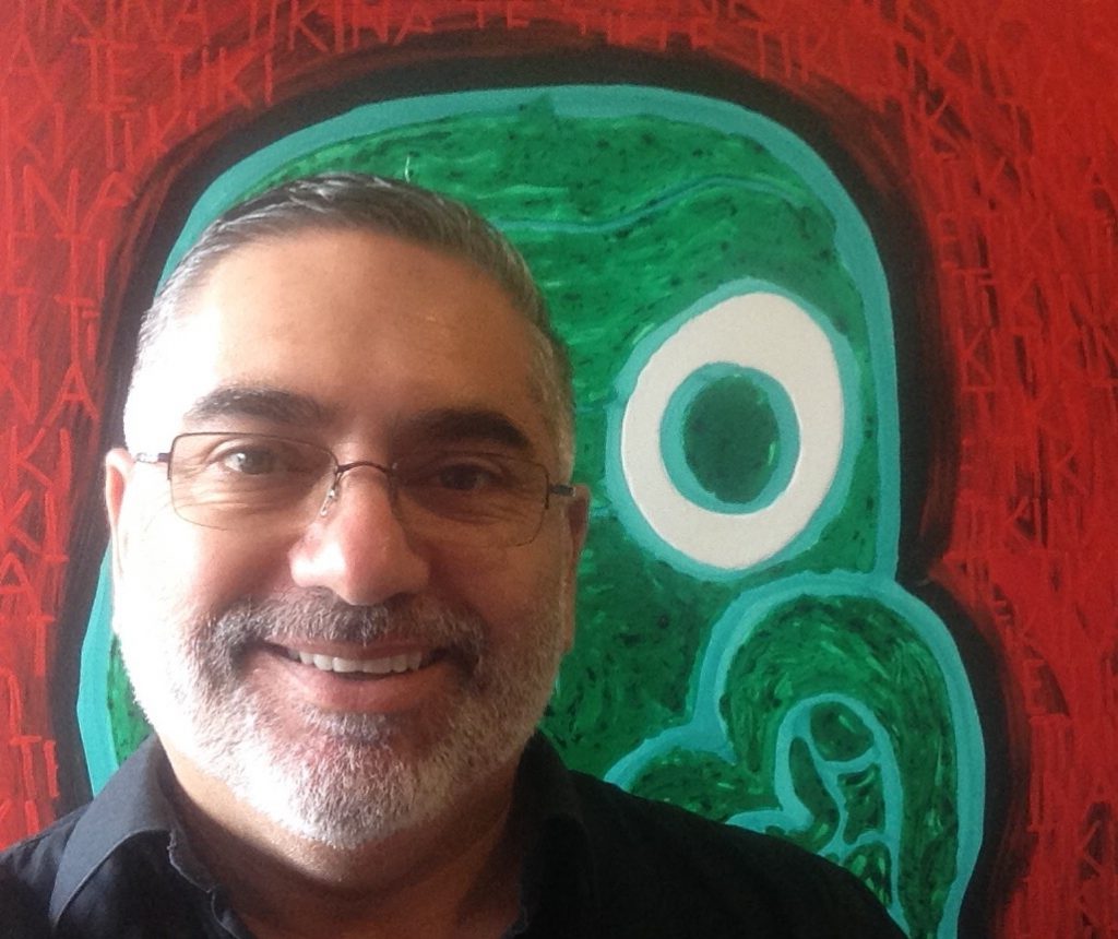 Head shot of Darryn Joseph. Behind him is one of his paintings of bold strokes in green and red.