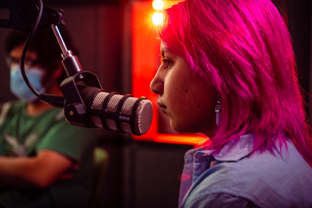 Teen with pink hair speaks into a microphone