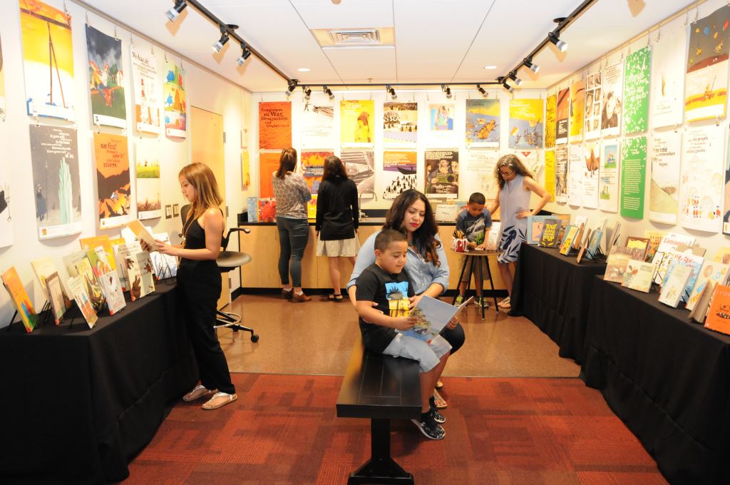 Patrons taking in WOW exhibit, Hello, Dear Enemy! on loan from the International Youth Library.