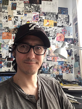Person with a friendly face wearing ballcap and glasses in front of a packed bulletin board
