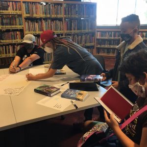 Four middle grade readers gathered around a table reading and writing recommended books on butcher paper.