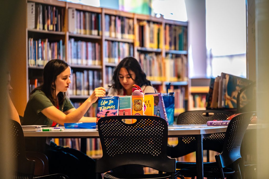 two middle school reading ambassadors browse a set of YA books