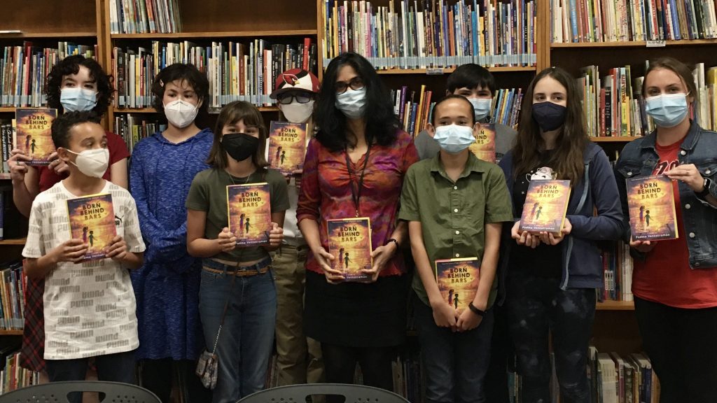 Author Padma Venkatraman stands in the center of middle schoolers holding copies of her book.