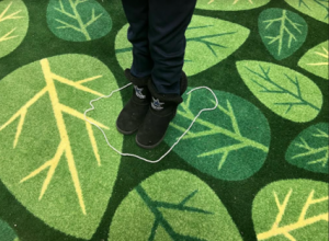 A child stands inside a small circle of yarn on top of a green carpet.