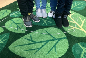 Four children stand together inside a larger yarn circle.